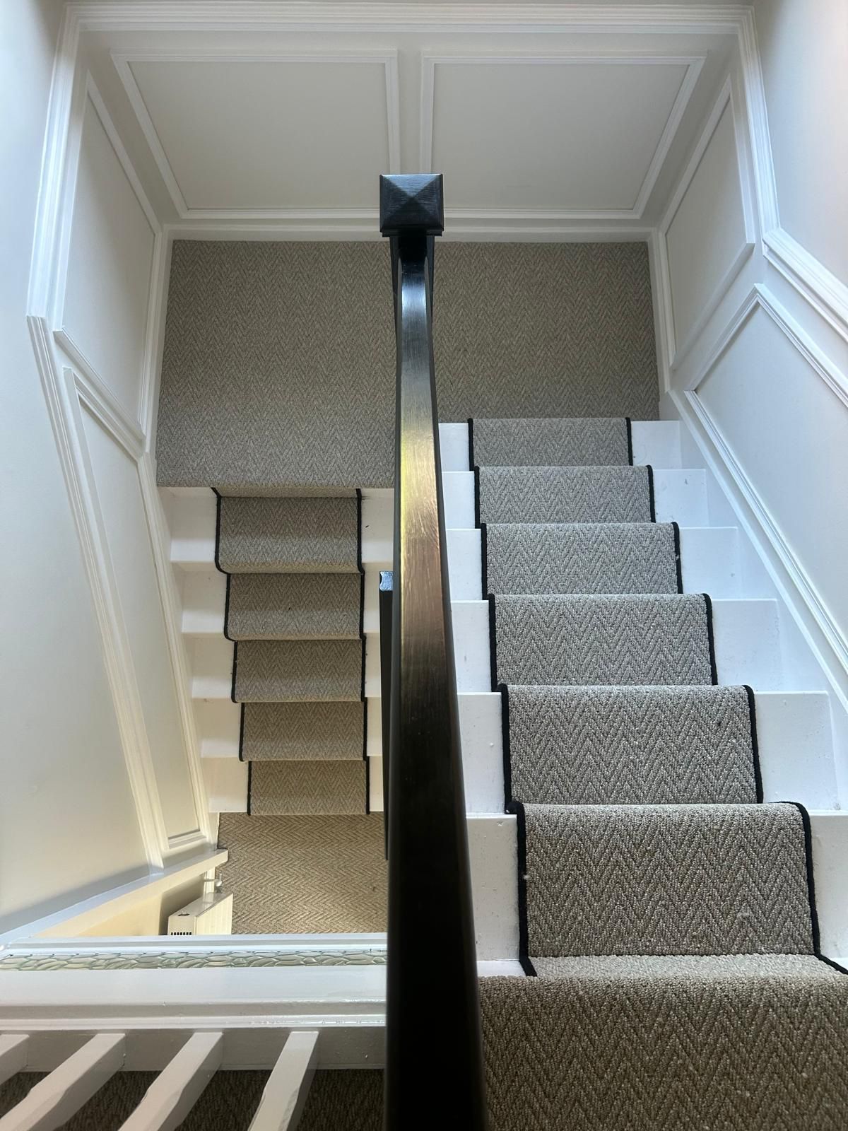 Staircase with a carpeted runner and a black handrail in a home interior.